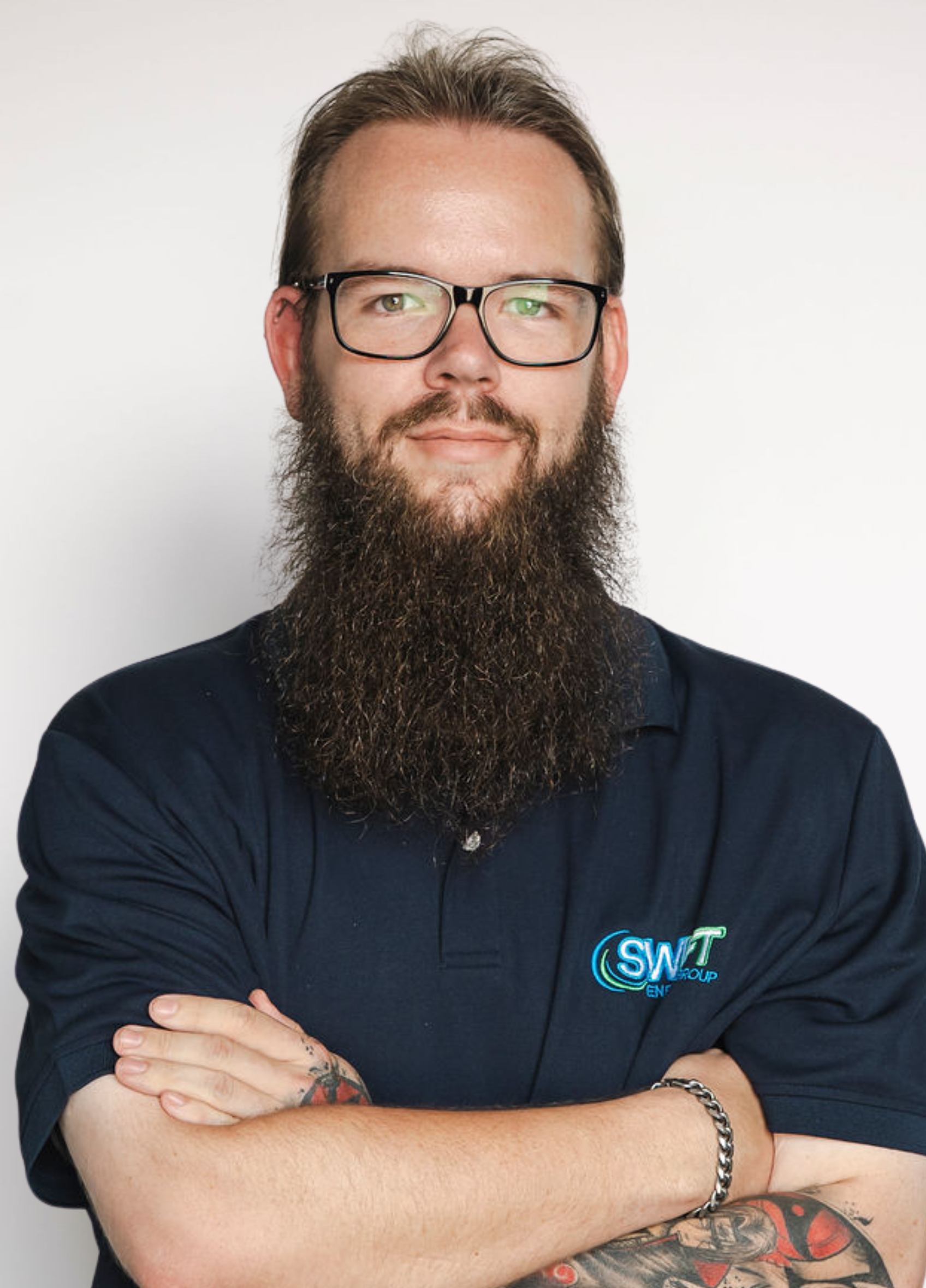 Bearded man with glasses and crossed arms wearing a dark polo shirt against a plain white background