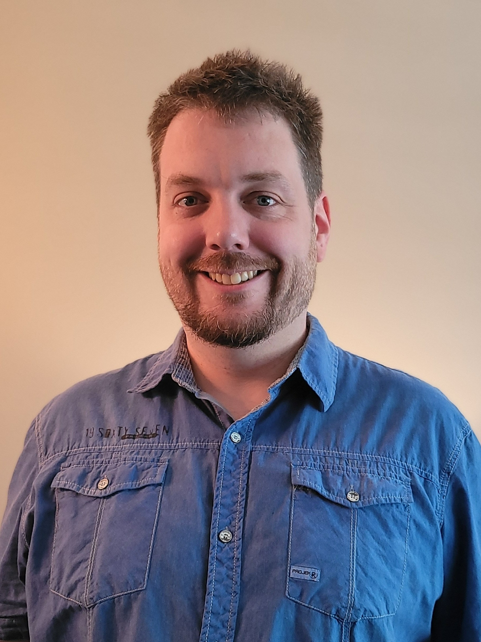 A man with a beard is wearing a blue shirt and smiling.