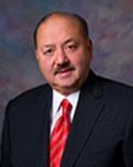 Man in suit and tie, red tie, dark background.