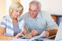 Senior couple reviewing finances together, using a calculator and laptop.