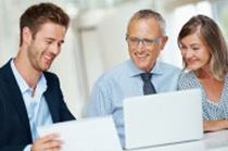 Smiling financial advisor showing documents and laptop to a couple in a bright office.