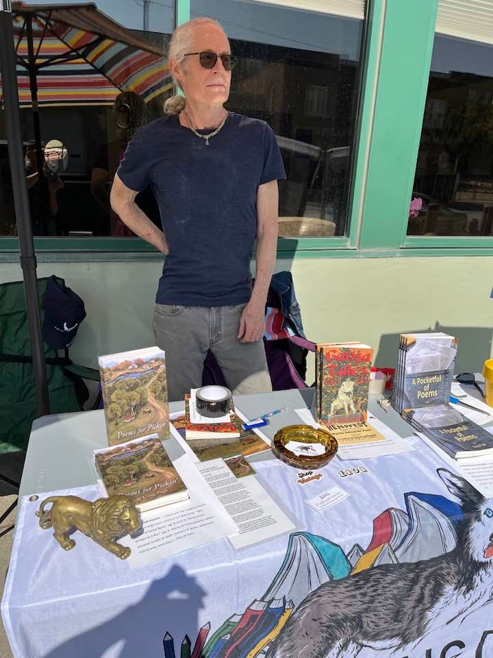 Vendor standing behind a table of artwork and items at an outdoor market booth
