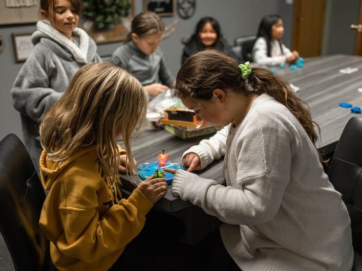 A group of young girls are sitting at a table making crafts.