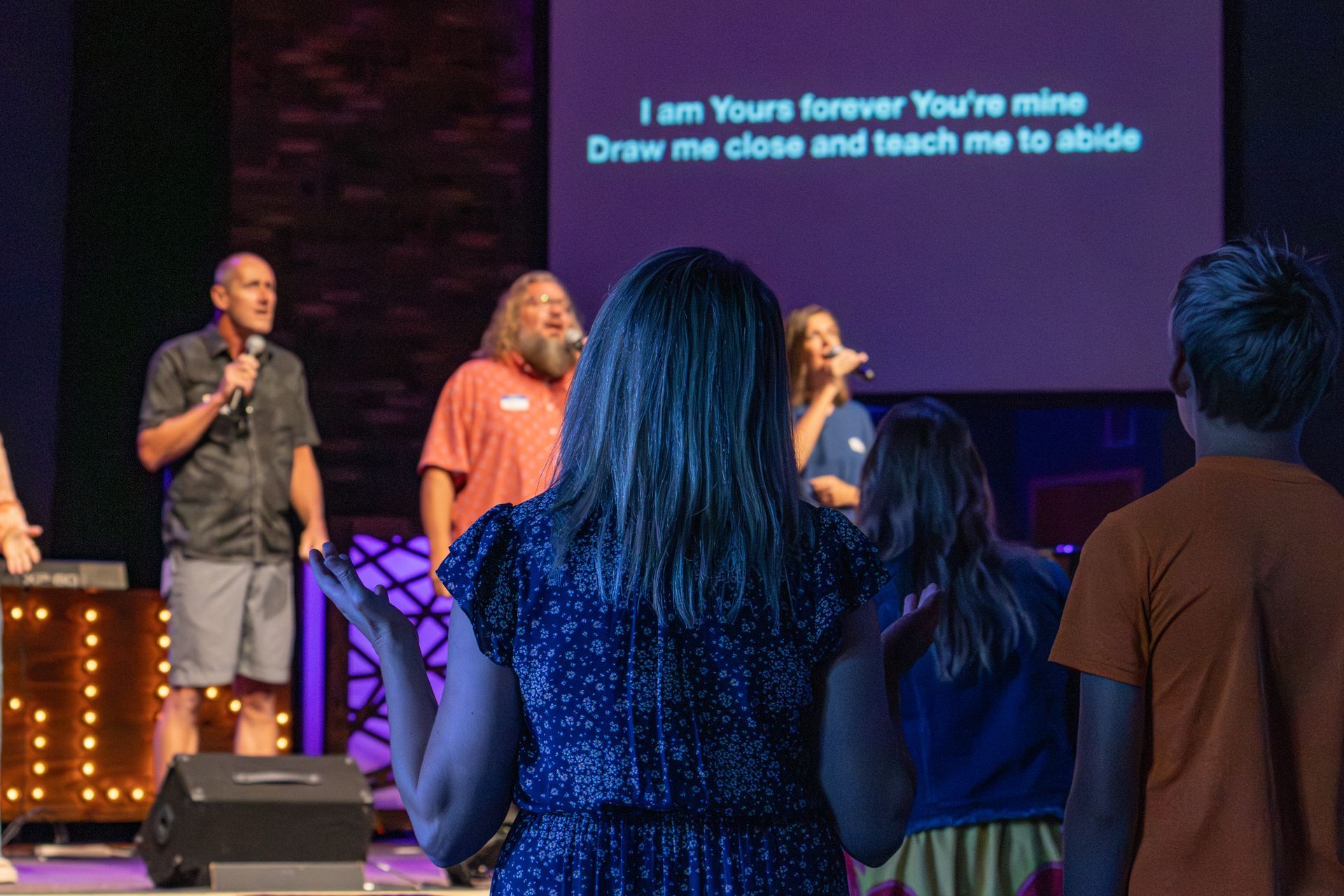 A group of people are singing into microphones on a stage.