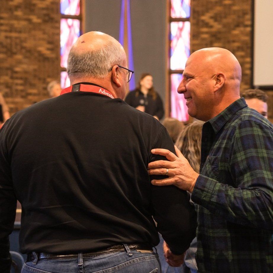 Two men are talking in front of a stained glass window