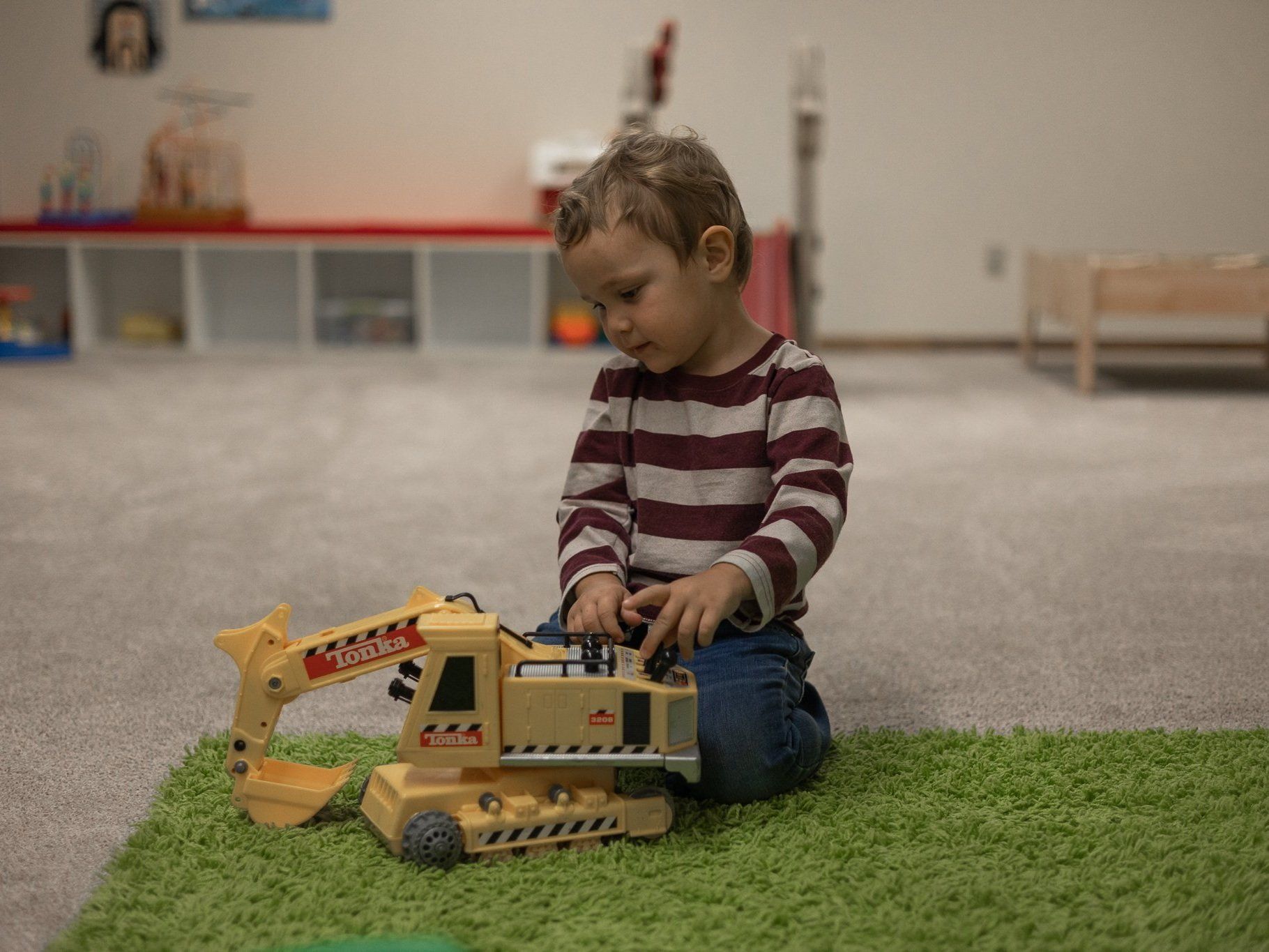 A young boy is sitting on the floor playing with a toy excavator.