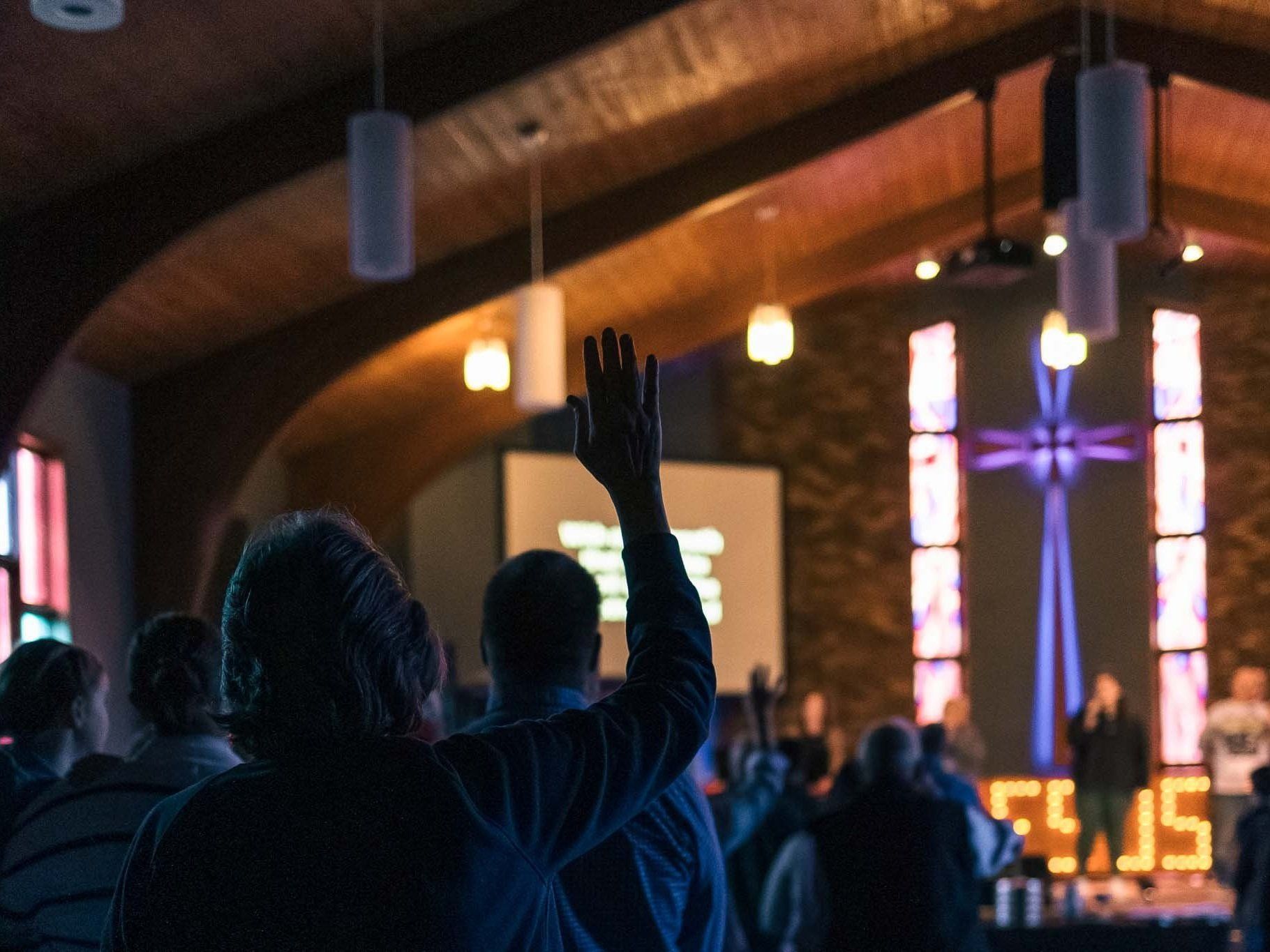A group of people are standing in a church with their hands in the air.