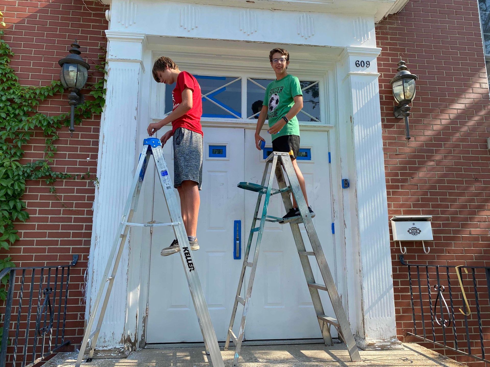 Two men are standing on ladders painting a door.