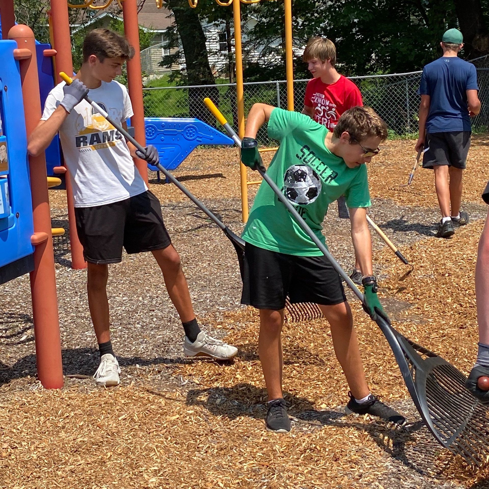 A group of young men are cleaning a playground with rakes and shovels.