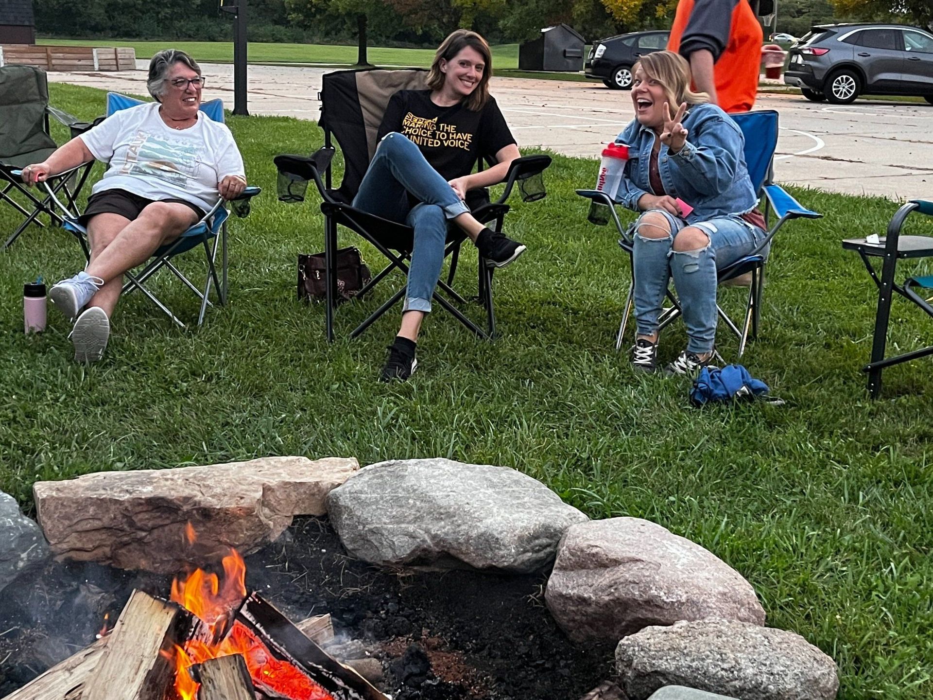 A group of people are sitting around a fire pit in the grass.