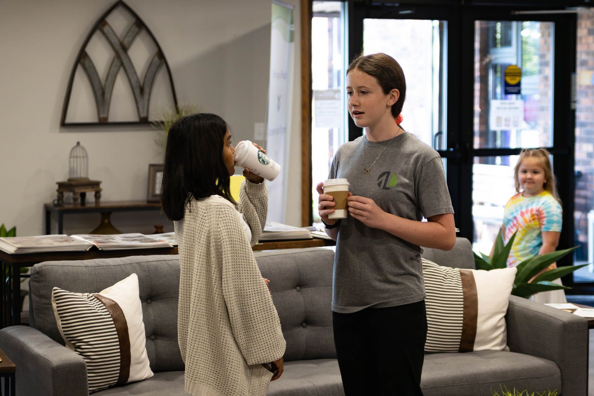 Two girls are standing next to each other on a couch in a living room.