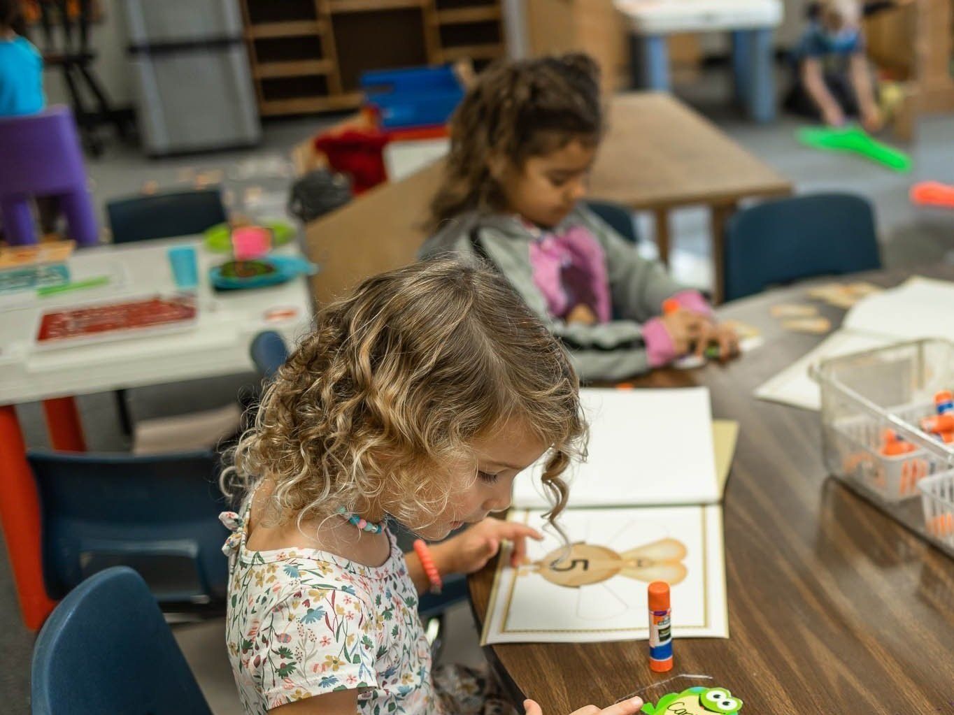 A little girl is sitting at a table in a classroom.