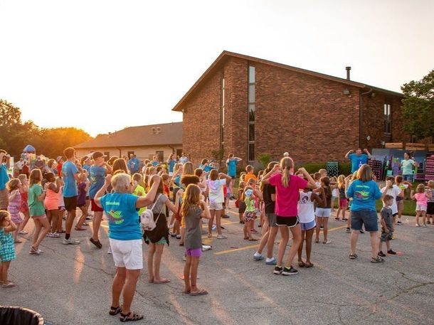 A large group of people are dancing in a parking lot in front of a brick building.