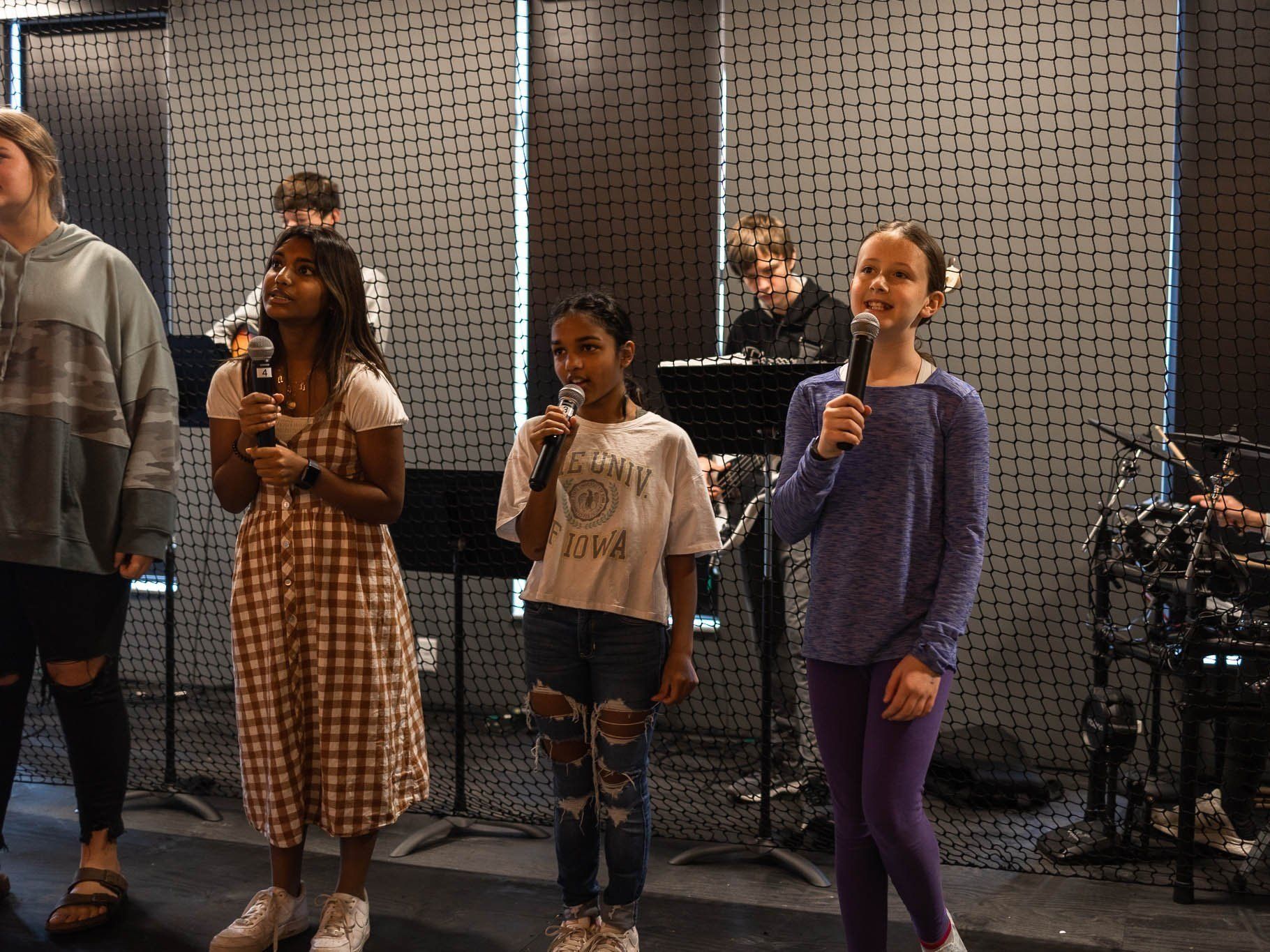 A group of young girls are singing into microphones in a room.