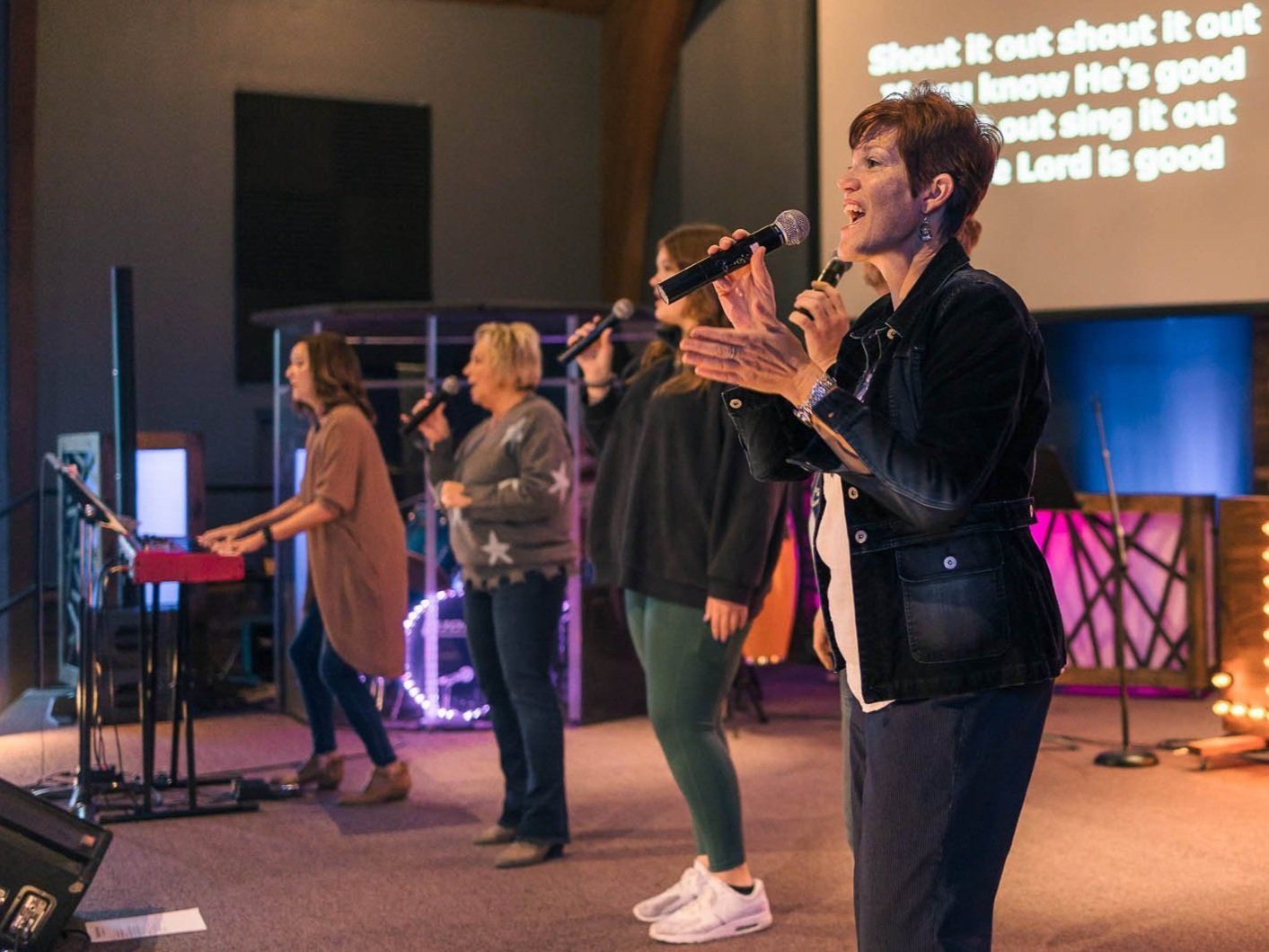 A group of women are singing into microphones on a stage.