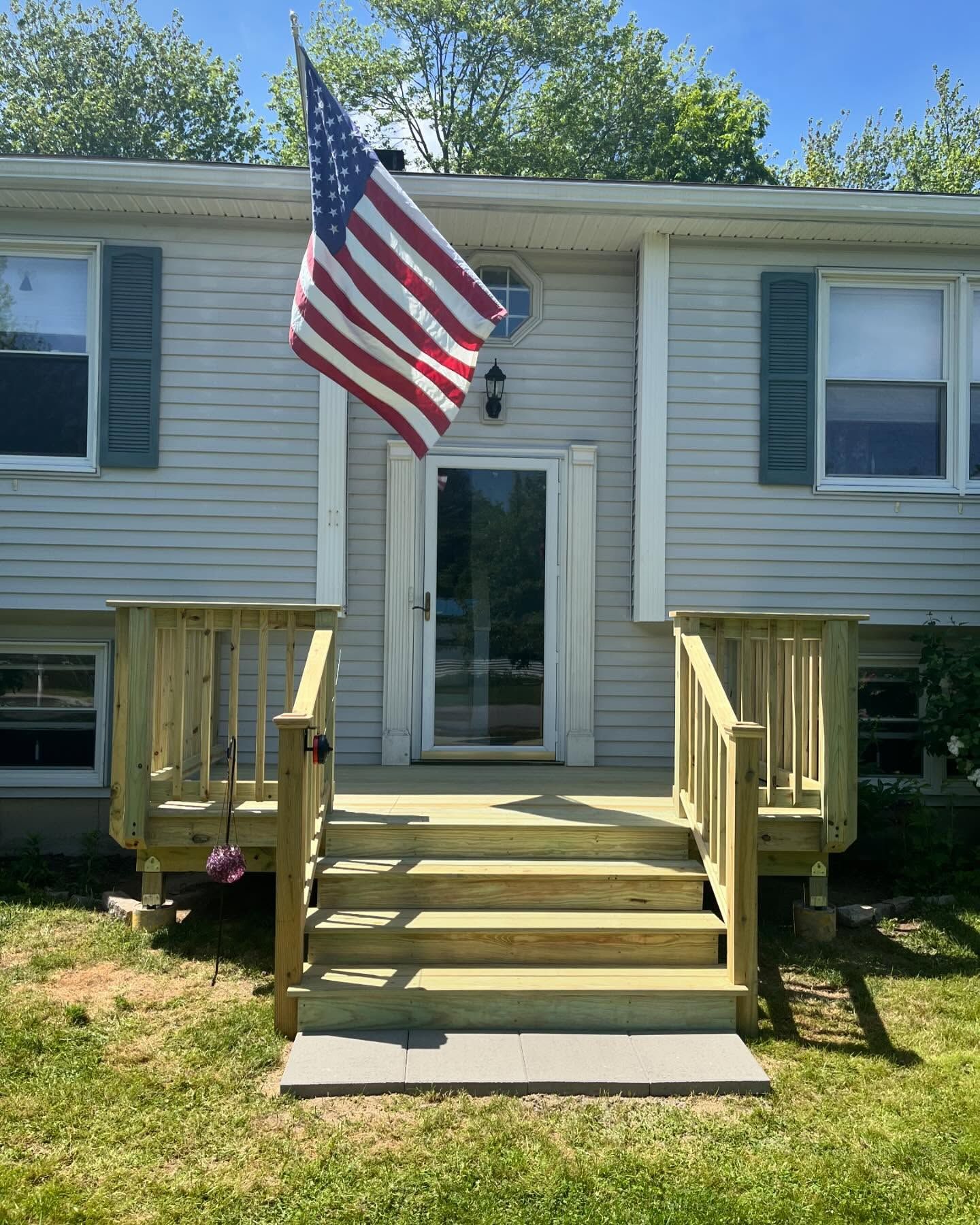 Wooden deck with stairs leading to a light-colored house. American flag hangs above the front door.