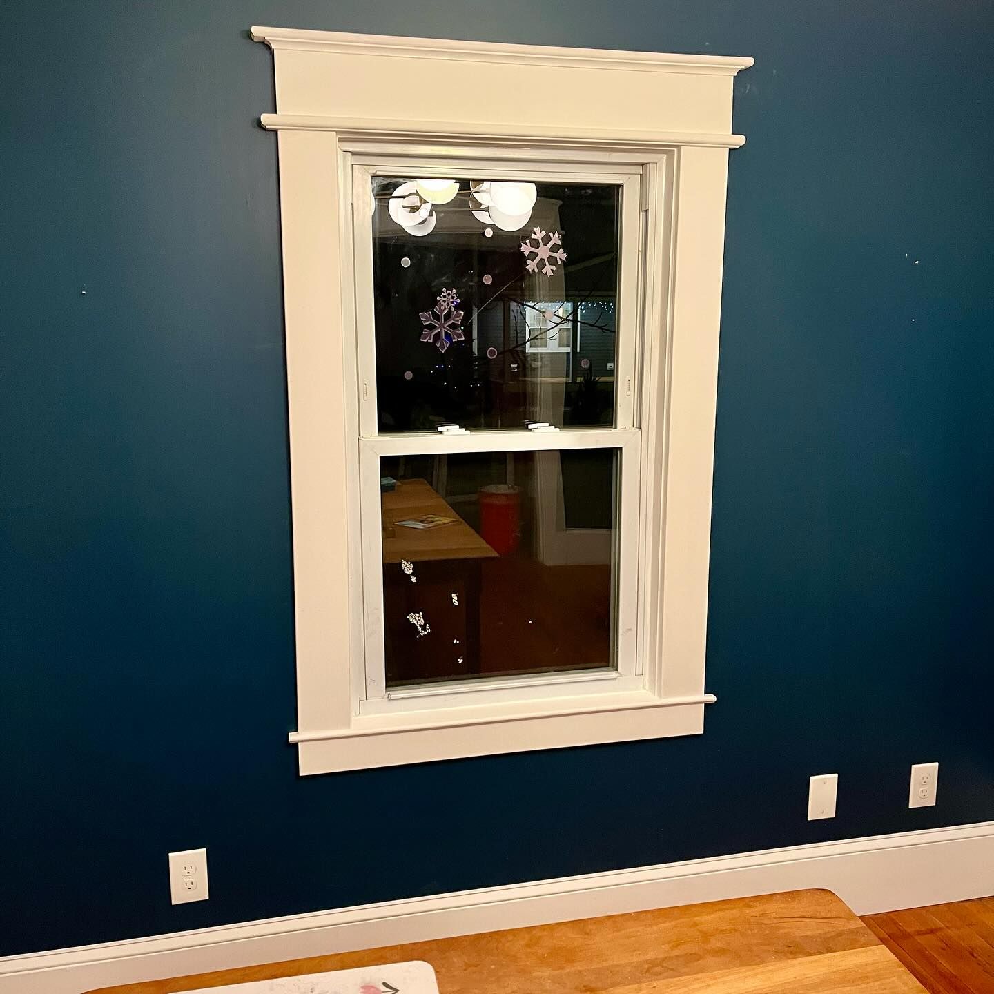 Window with white trim against a dark blue wall. Snowflakes decorate the glass.