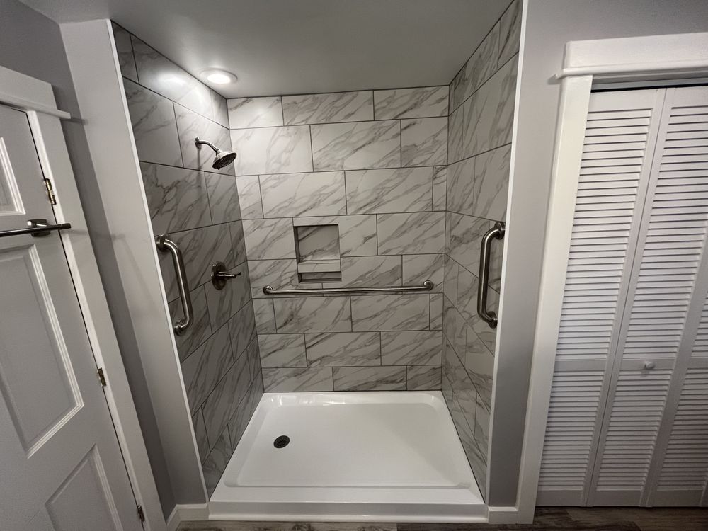 Accessible shower with white tiled walls, grab bars, and a built-in shelf.