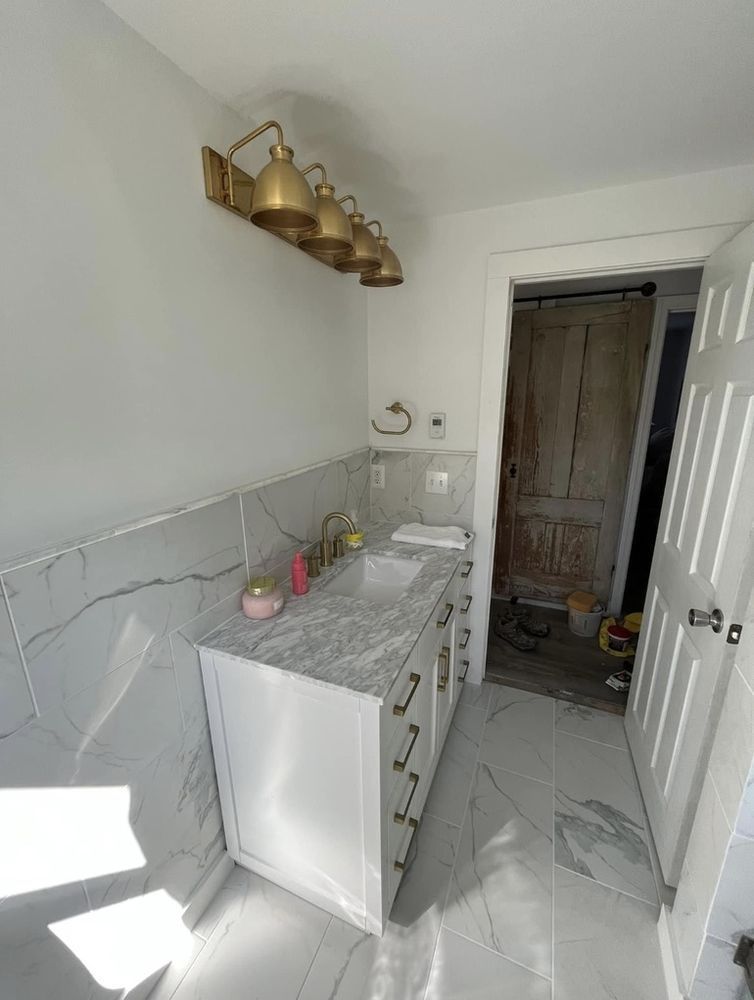 Bathroom with white vanity, marble-look tile, gold fixtures, and a rustic wooden door.