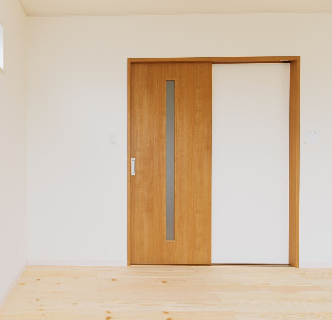 Wooden sliding door partially open, set in a white wall with light wooden flooring.