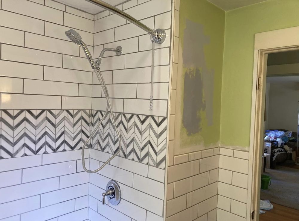 Bathroom with white subway tile and chevron accent. Shower head, faucet, and green wall with grey patch.