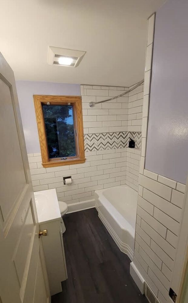 Small bathroom with white subway tile, a bathtub, and dark wood flooring.