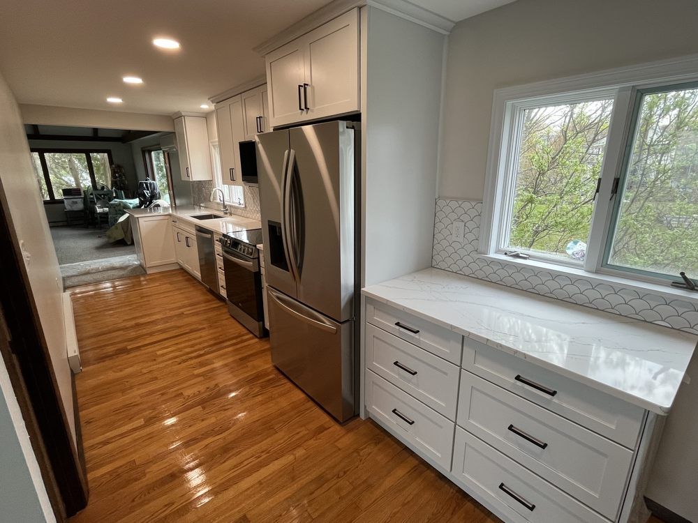 White kitchen with stainless steel appliances, wood floors, and a window.