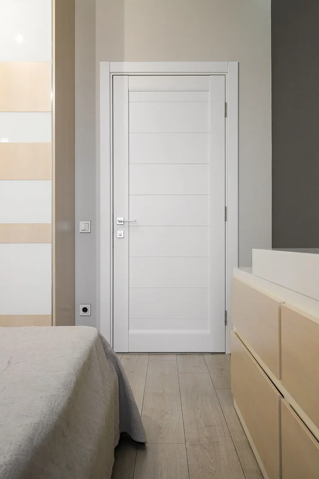 White interior door in a neutral-toned room; part of a bed, closet, and dresser are also visible.