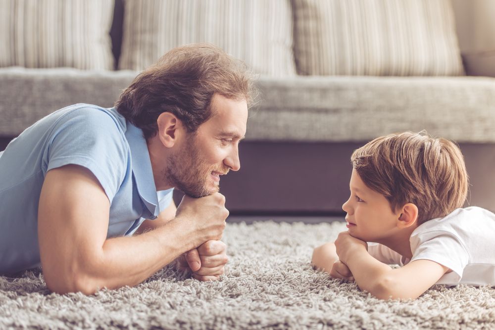 A father and son are laying on the floor talking to each other.