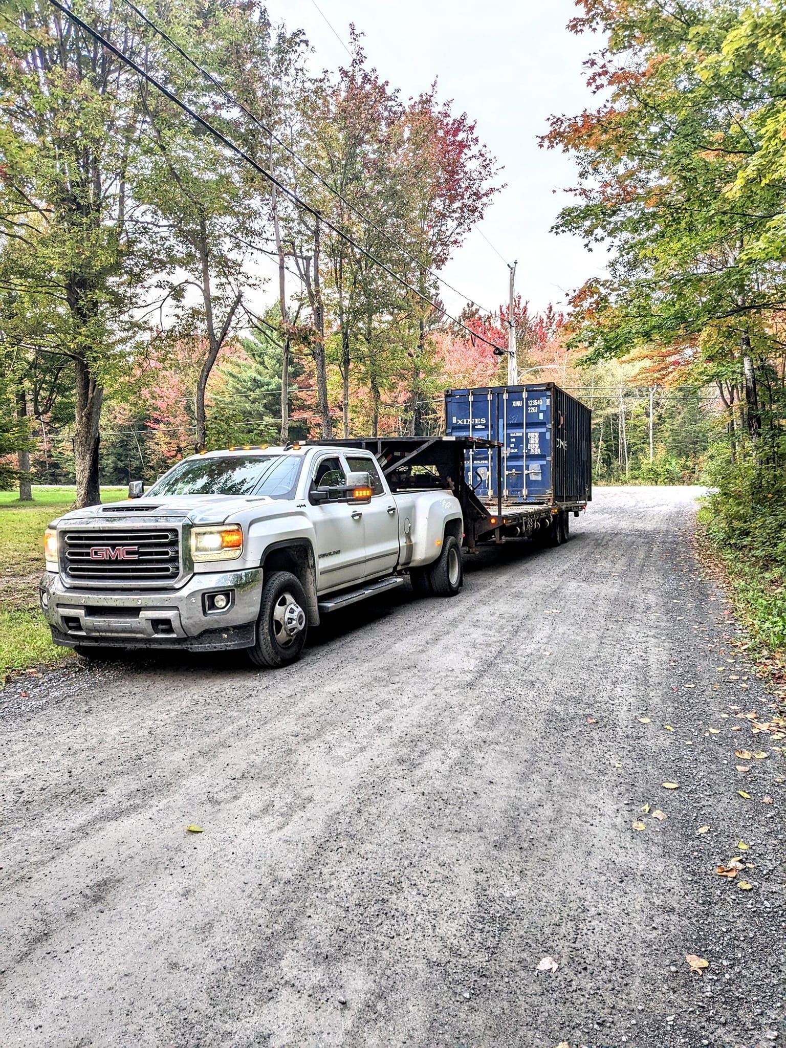 Un camion remorque un conteneur bleu sur une route de gravier.