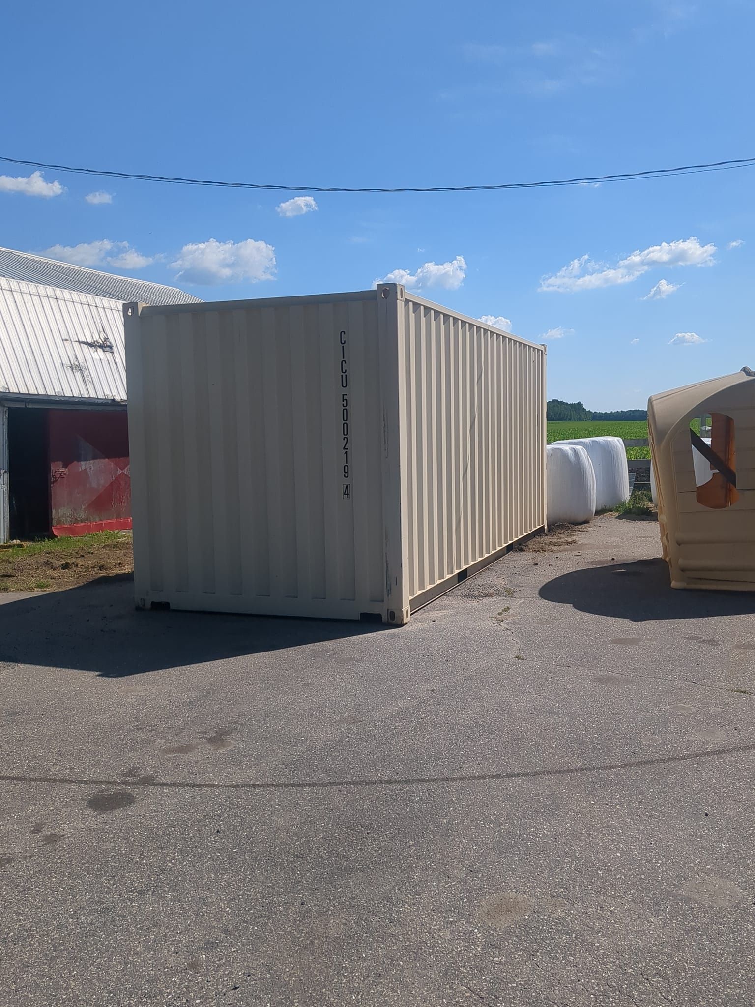 Un conteneur d'expédition blanc est assis sur un parking à côté d'un tas de foin.