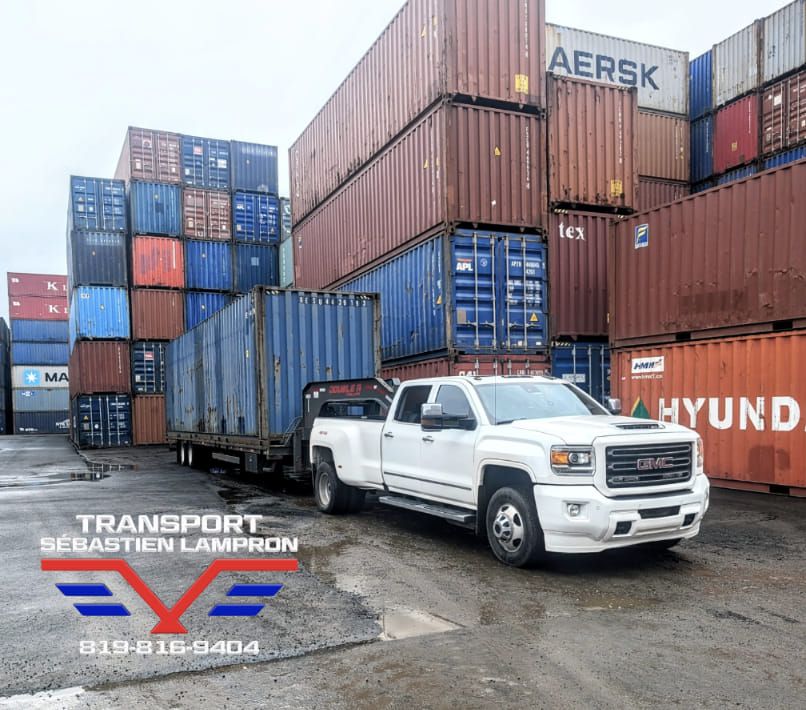 Un camion blanc est garé devant une pile de conteneurs d'expédition.