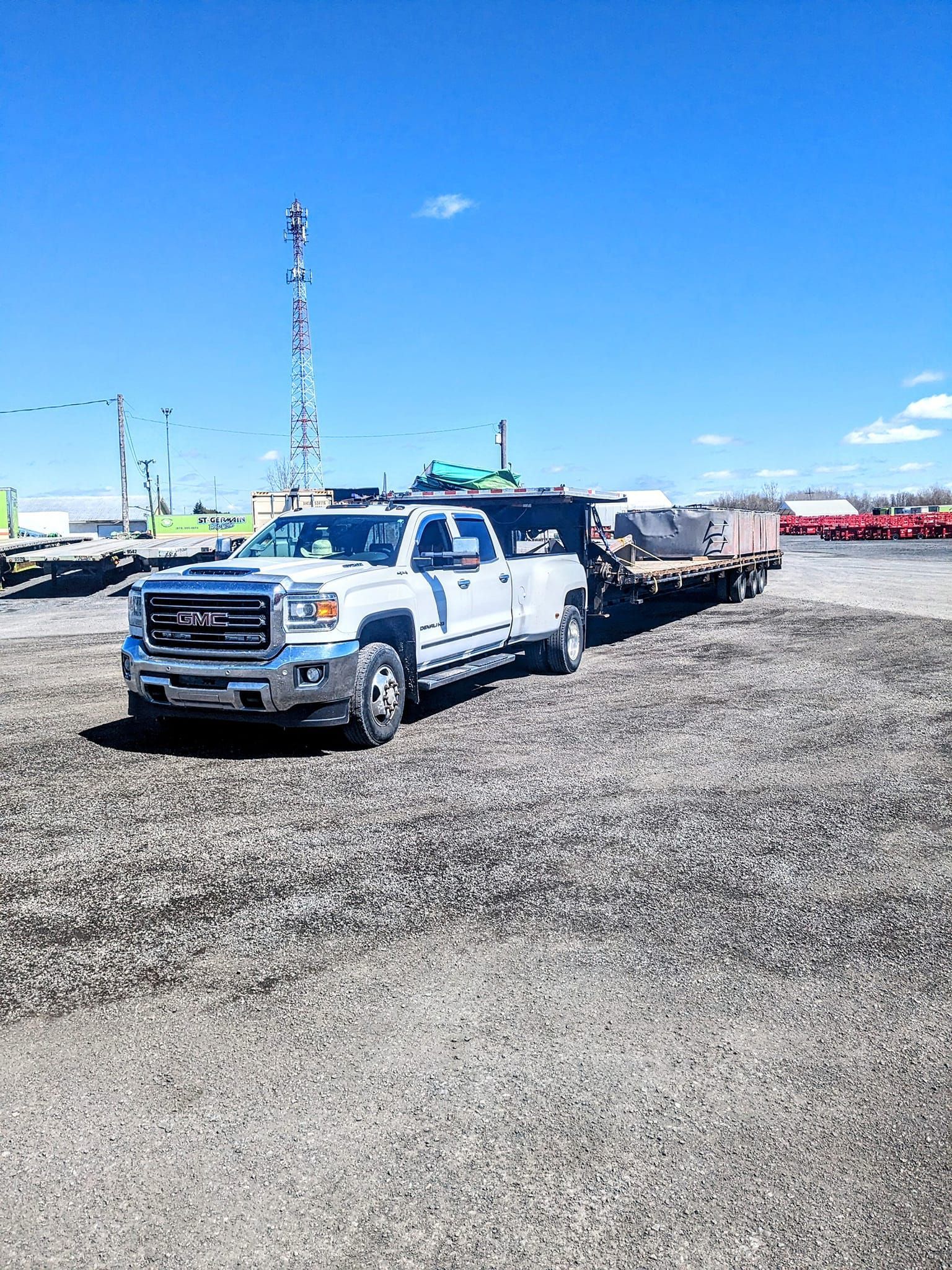 Un camion blanc est garé sur un terrain en gravier à côté d'une remorque.