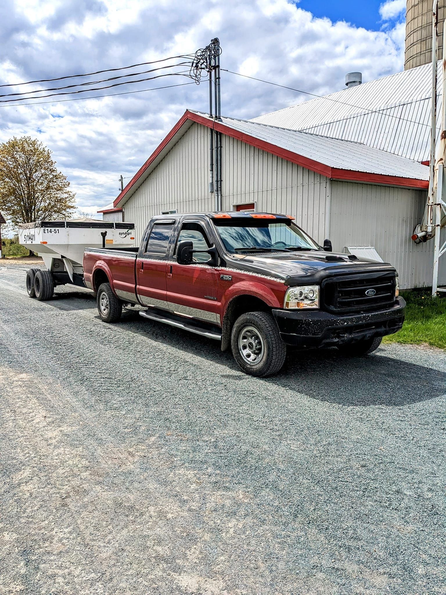 Un camion rouge tire une remorque sur une route de gravier.