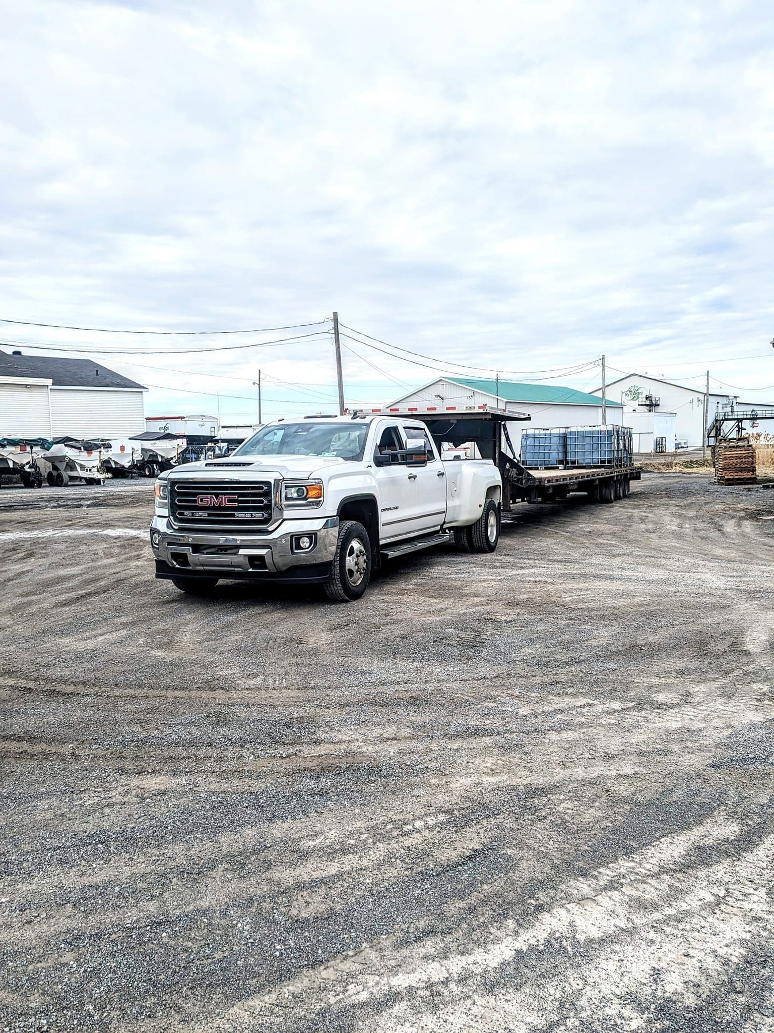 Un camion blanc tracte une remorque sur un terrain en gravier.
