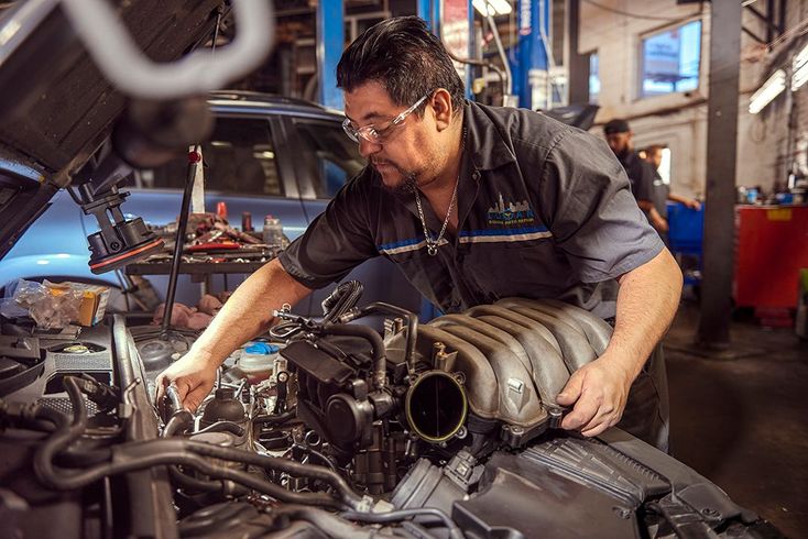 Mechanic working on a car engine in a garage, tightening parts near a large turbocharger.