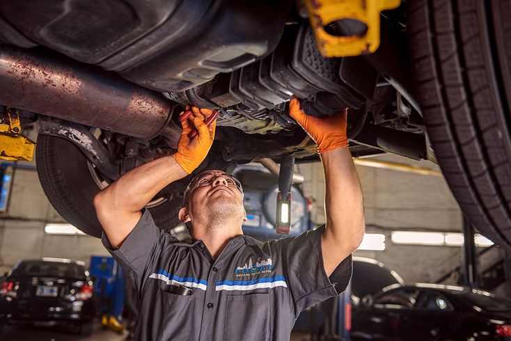 Mechanic in orange gloves repairs a car’s undercarriage in a garage