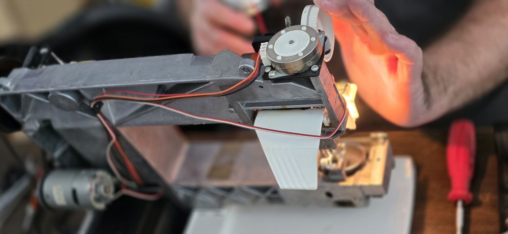 Een persoon werkt aan de interne onderdelen van een machine. Handen, draden, een schroevendraaier en een motor zijn zichtbaar