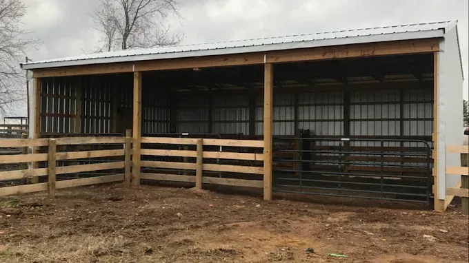 Open-air horse shelter with metal roof and wooden fencing.