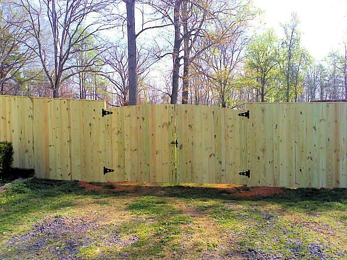 Wooden fence with a gate in a grassy yard, trees in the background.