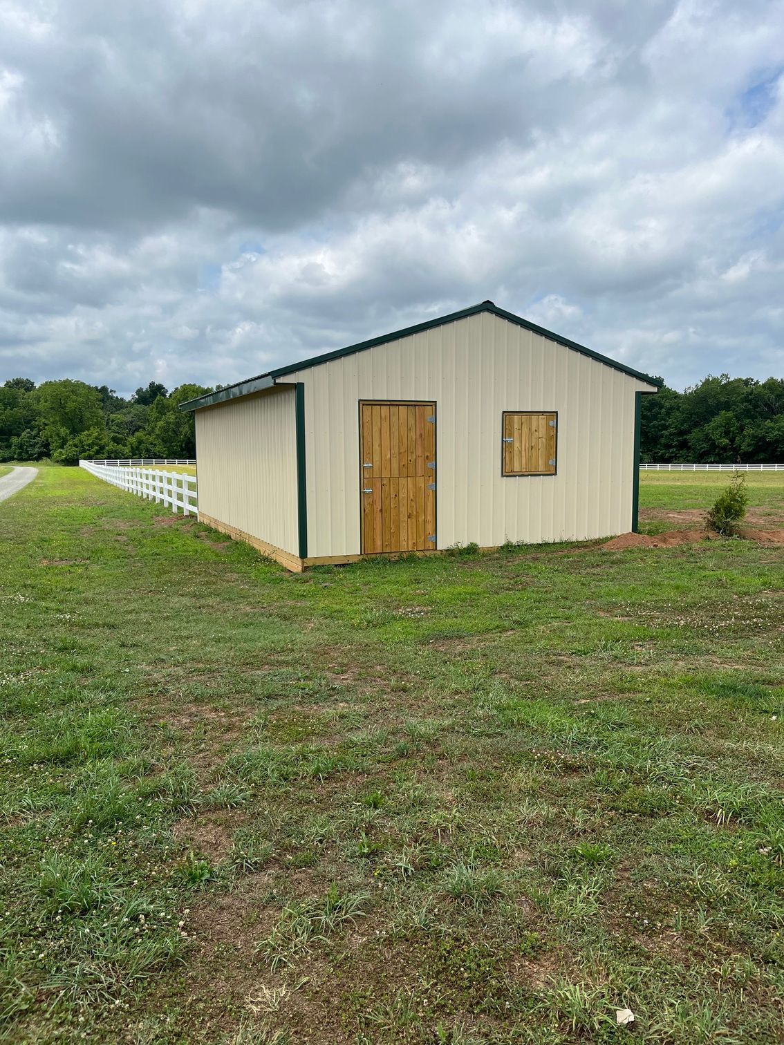Tan metal shed with green trim, wooden door and window, on a grassy hill.