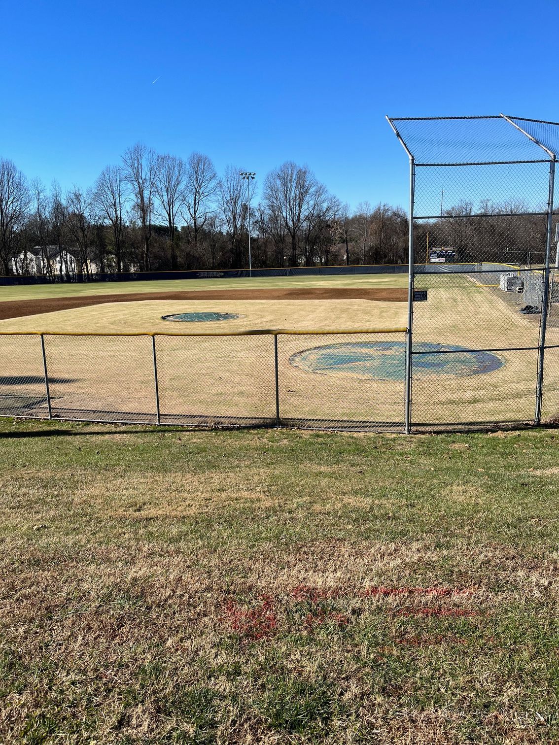 Baseball field, fenced, with bare trees under a clear, blue sky.