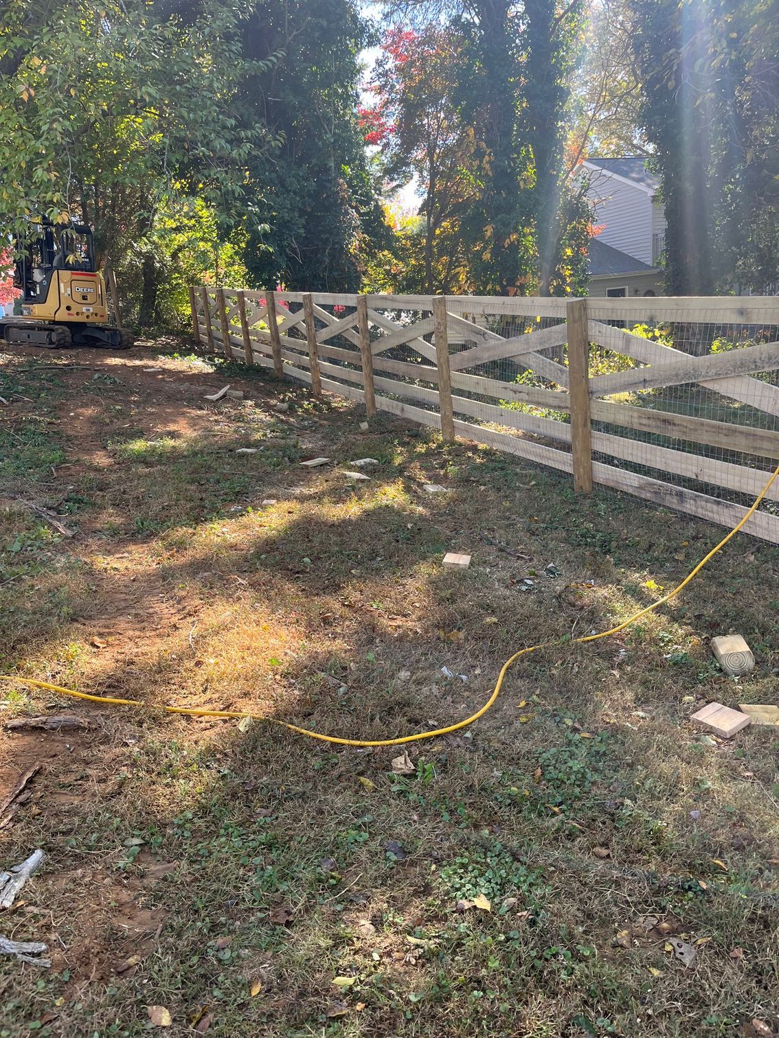 A wooden fence with an x-pattern being built in a grassy backyard near trees.