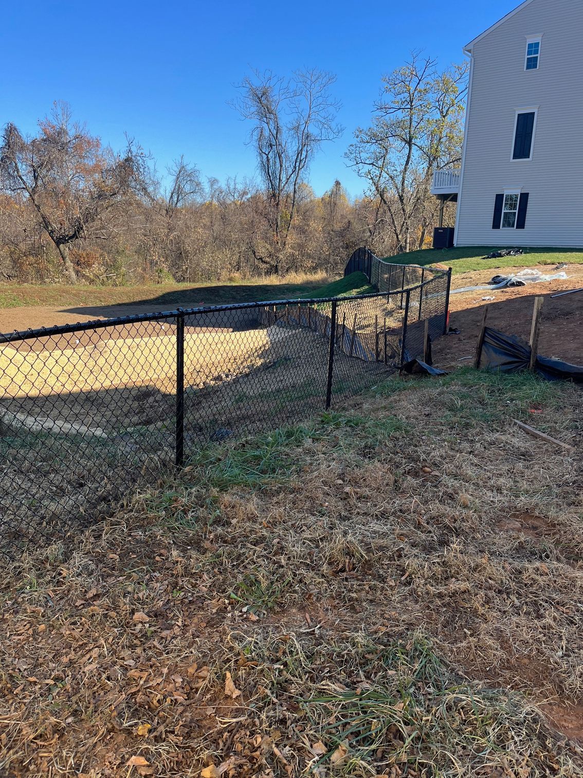 Black chain-link fence in yard with brown grass, leading towards a building.