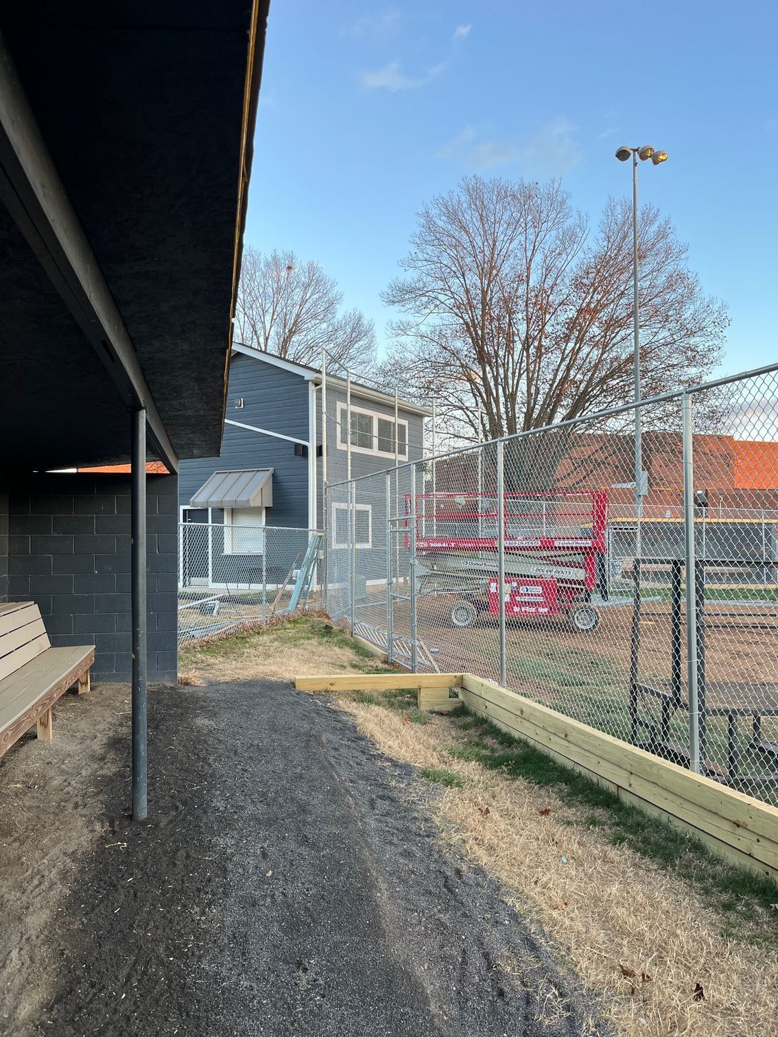 Baseball dugout with a chain-link fence and a building in the background.