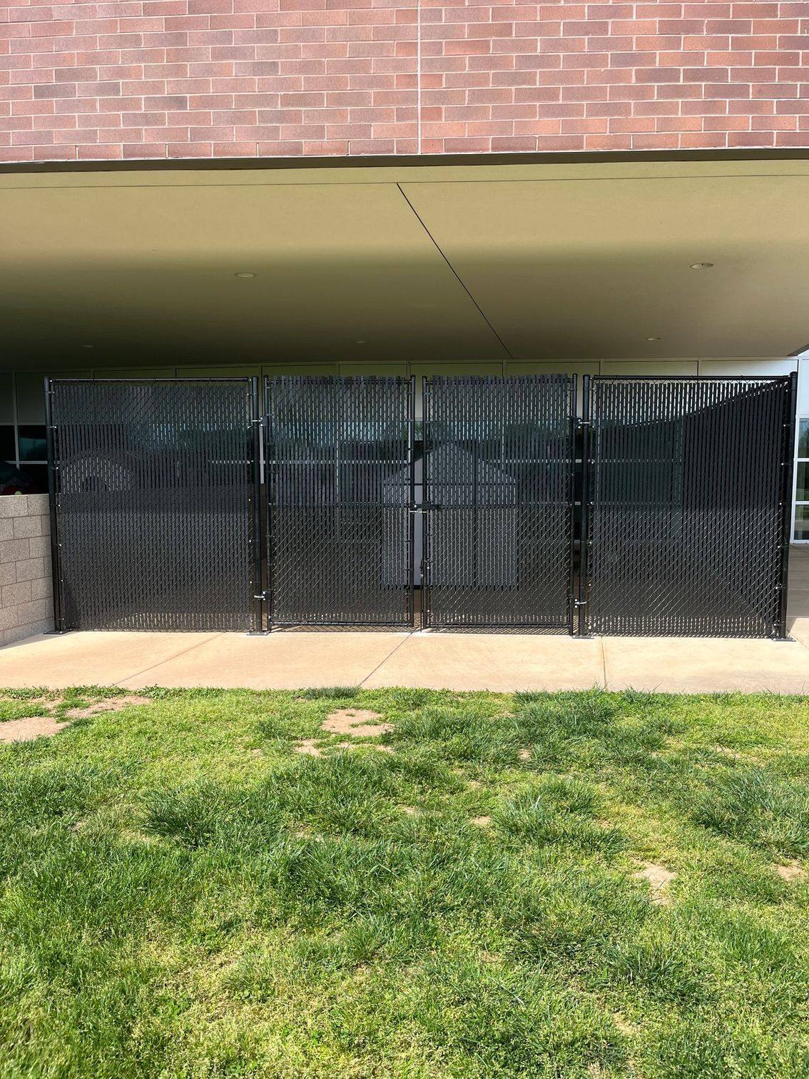 Black metal fence in front of a brick building with green grass in the foreground.
