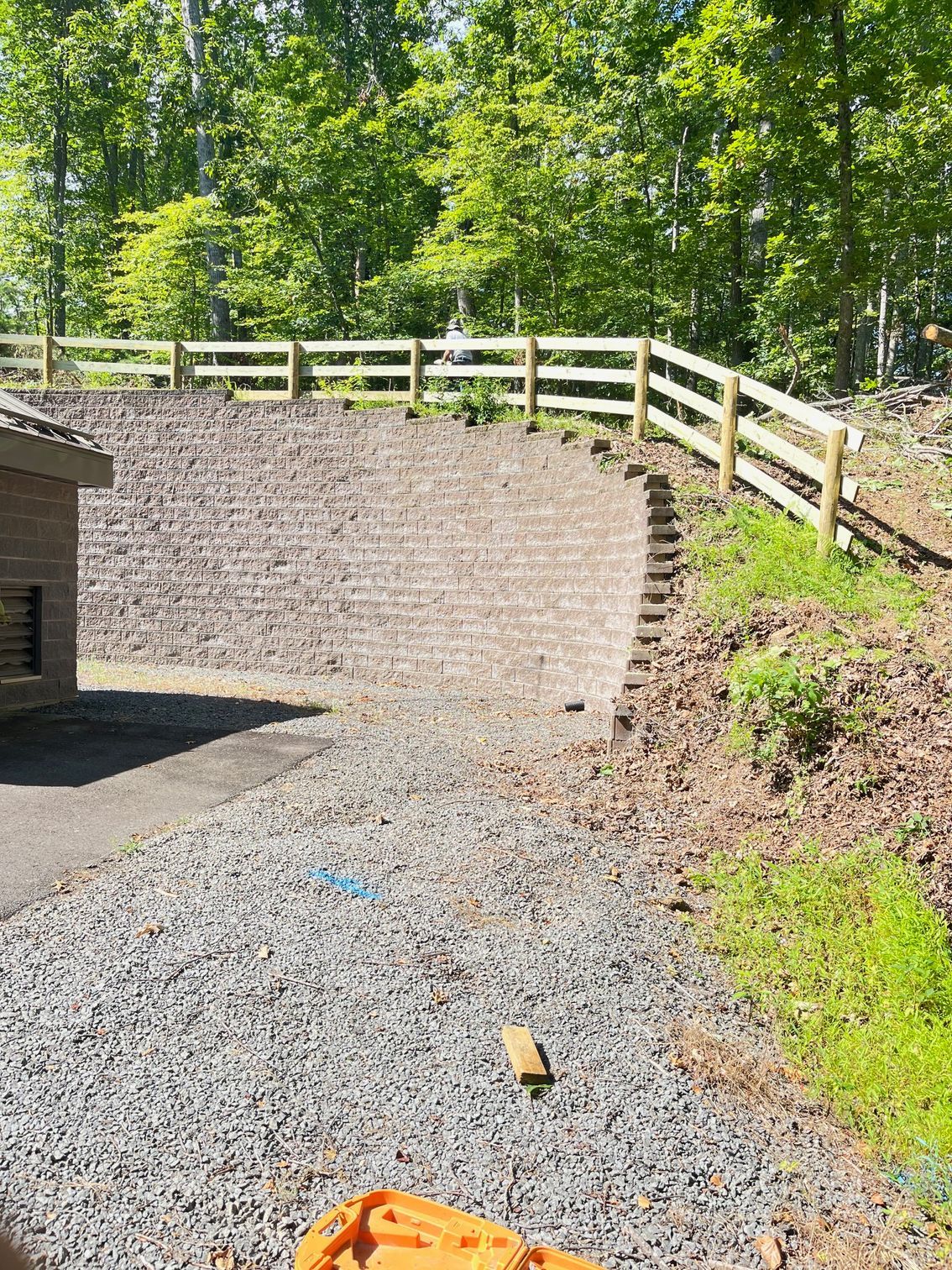 A gravel driveway leads to a retaining wall topped with a wooden fence.