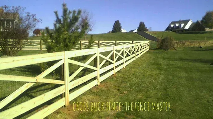 Wooden cross buck fence on a grassy hill in front of houses.