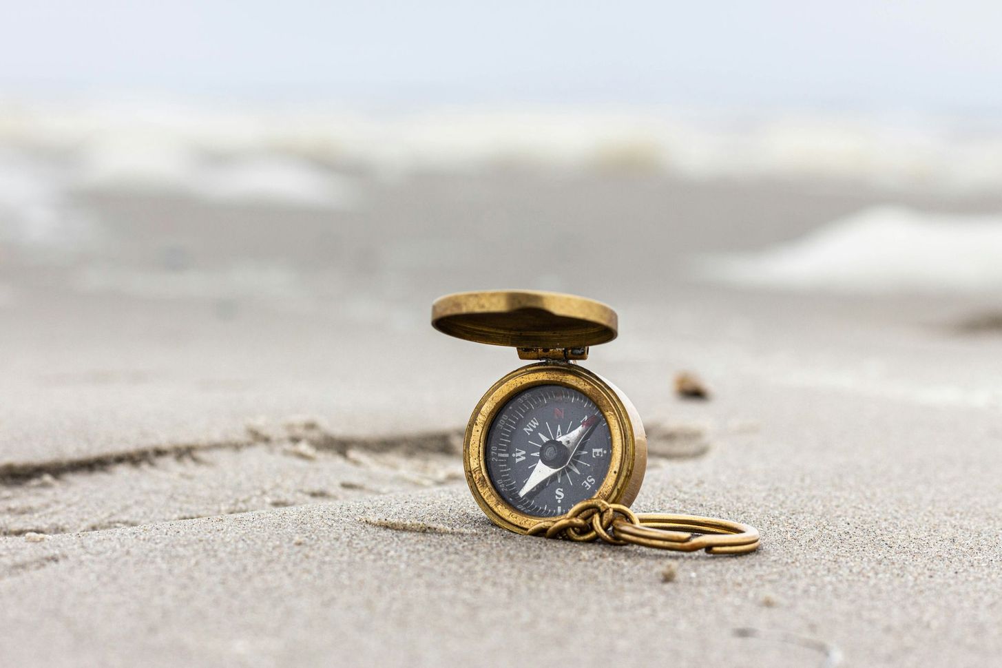 Gold pocket watch lying open on a sandy beach with blurred waves in the background