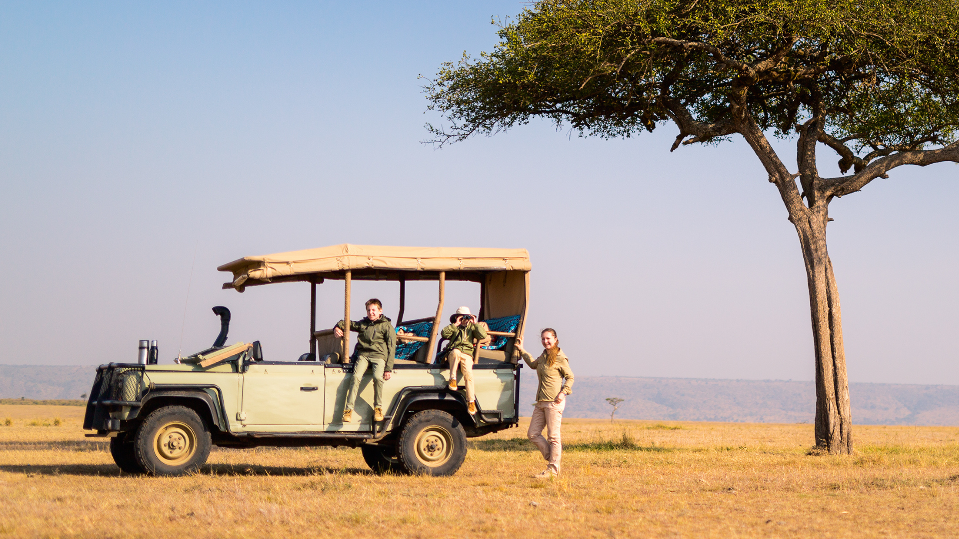 A couple of people standing next to a jeep in a field.